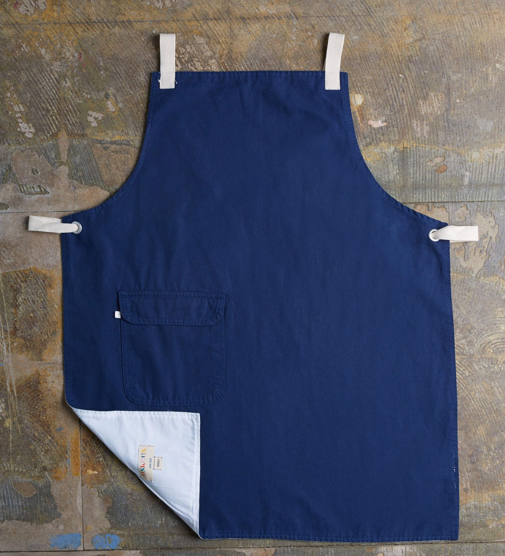 Full, flat view of navy #9001 work apron by Uskees. Showing hip pocket with left corner folded up to reveal lining and 'Uskees' label.