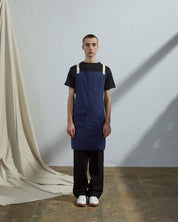 Full-length, front view of male model wearing Uskees #9001 navy work apron by Uskees. Showing convenient hip pocket and contrasting cream straps.