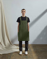 Full-length, front view of model wearing Uskees #9003 army green Japanese style apron by Uskees. Showing deep side pockets.