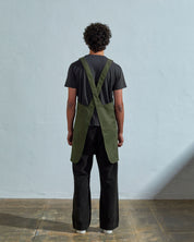 Full-length, rear view of model wearing Uskees #9003 coriander-green Japanese-style apron by Uskees. Clear view of cross back design.