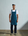 Full-length, front view of model wearing Uskees #9003 peacock blue-green Japanese style apron by Uskees. Showing deep side pockets.