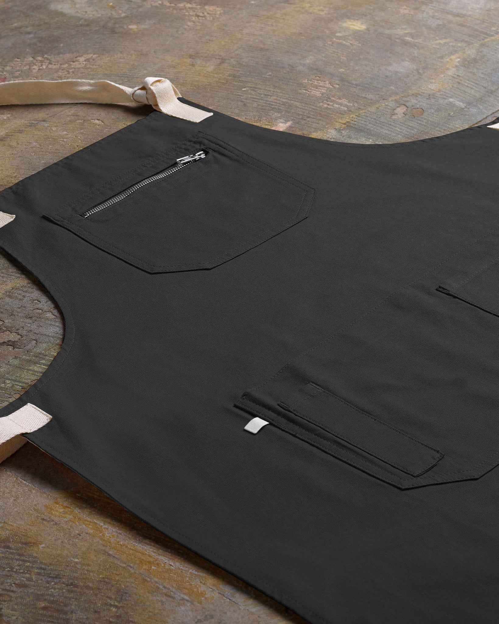 Angled flat view of faded black #9004 carpenter apron by Uskees. Showing pen, phone and pouch pockets and clearer view of organic cotton fabric texture.