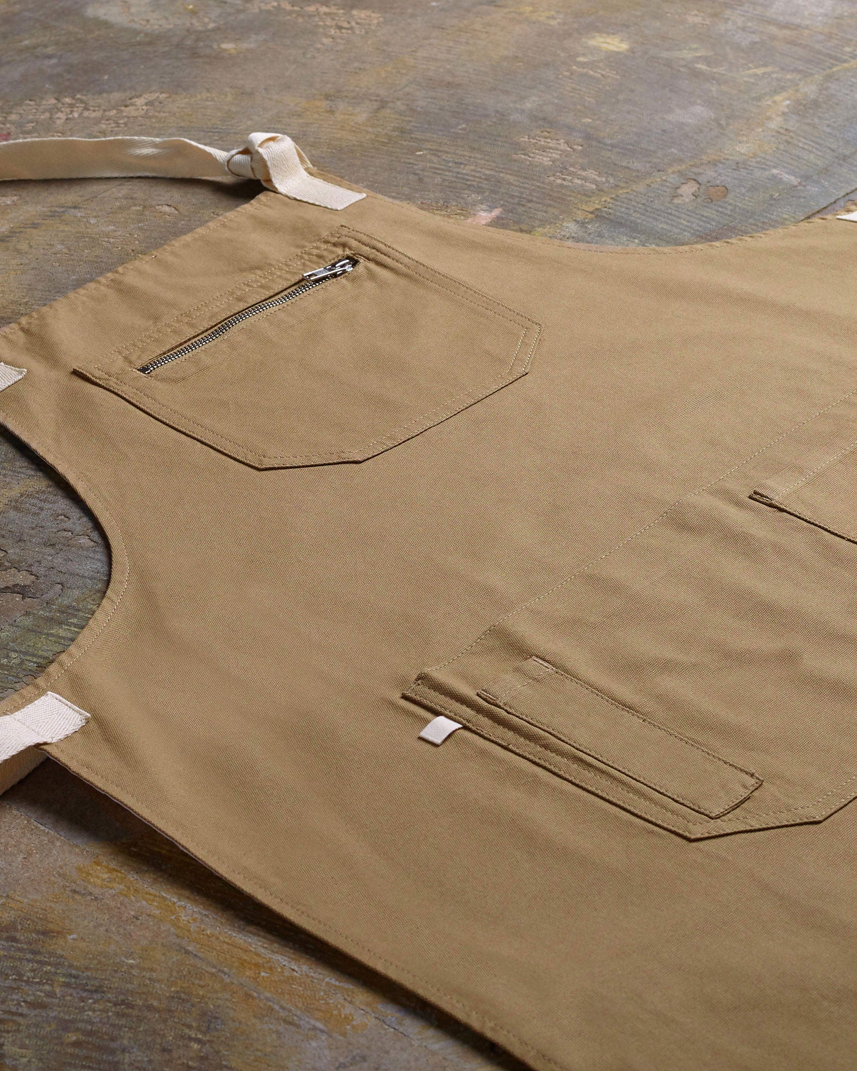 Angled flat view of khaki #9004 carpenter apron by Uskees. Showing pen, phone and pouch pockets and clearer view of organic cotton fabric texture.