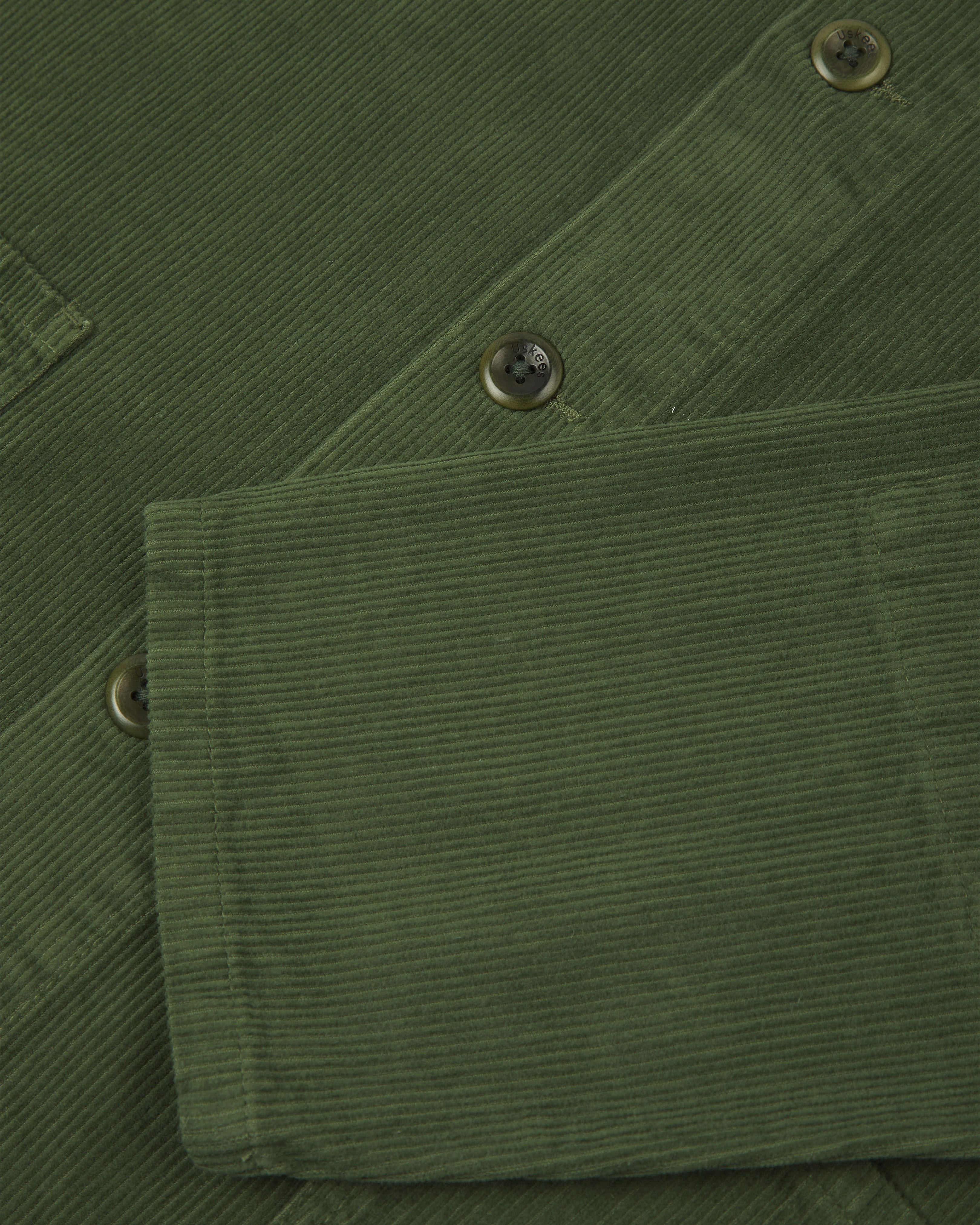 Front close shot of mid-green, buttoned corduroy overshirt from Uskees. Clear view of green corozo buttons and sleeve