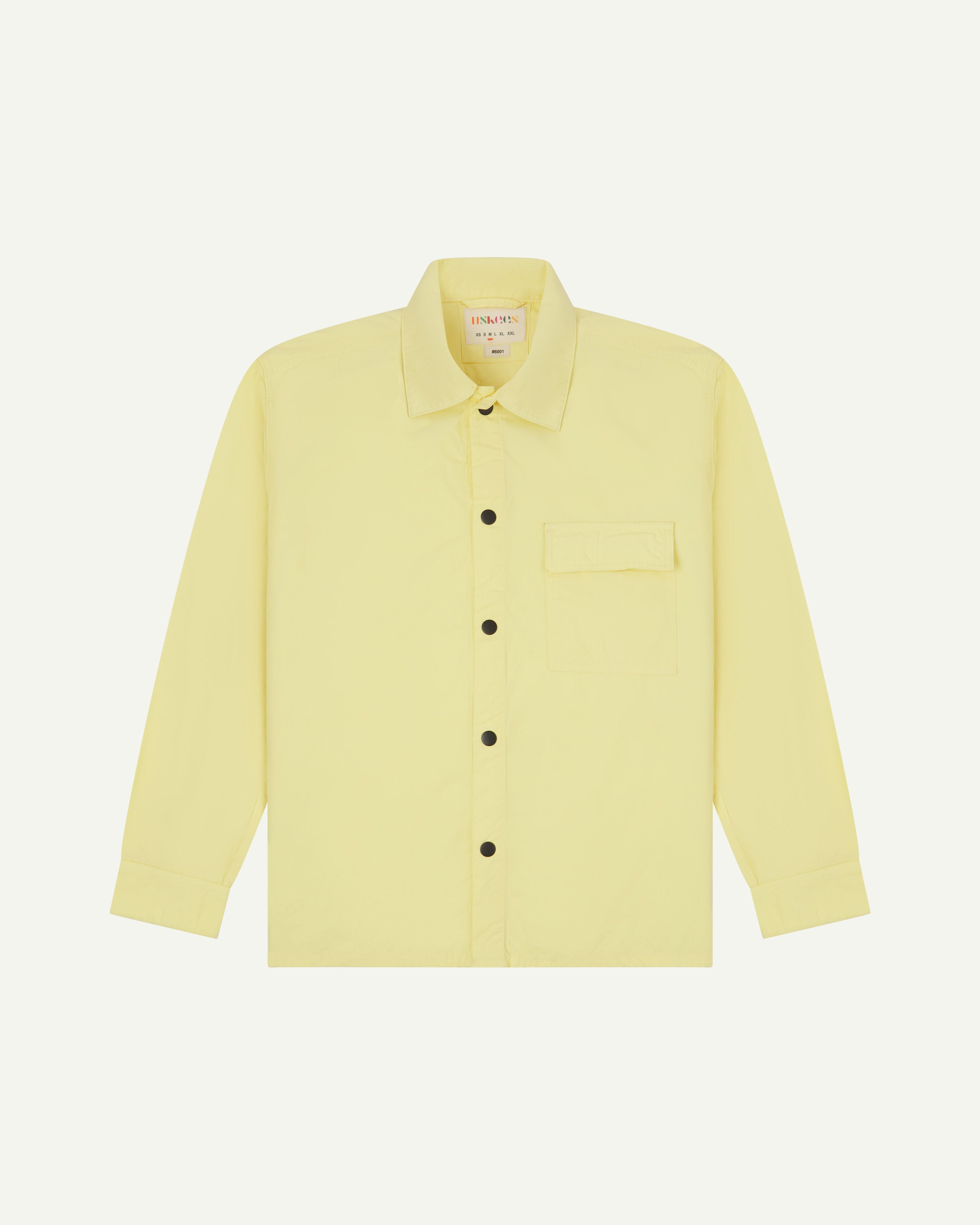 Front-view of pale yellow buttoned lightweight overshirt from Uskees. Clear view of breast pocket, black press studs and sharp detailing.