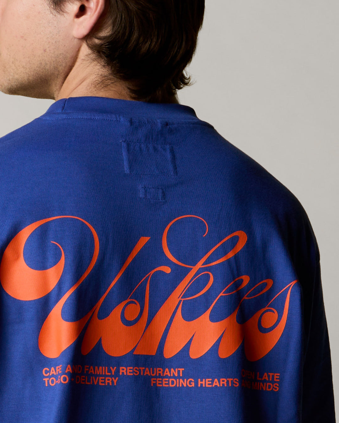back view close up shot of model wearing  the uskees men's graphic Tee in ultra blue showing the 'diner' logo in orange