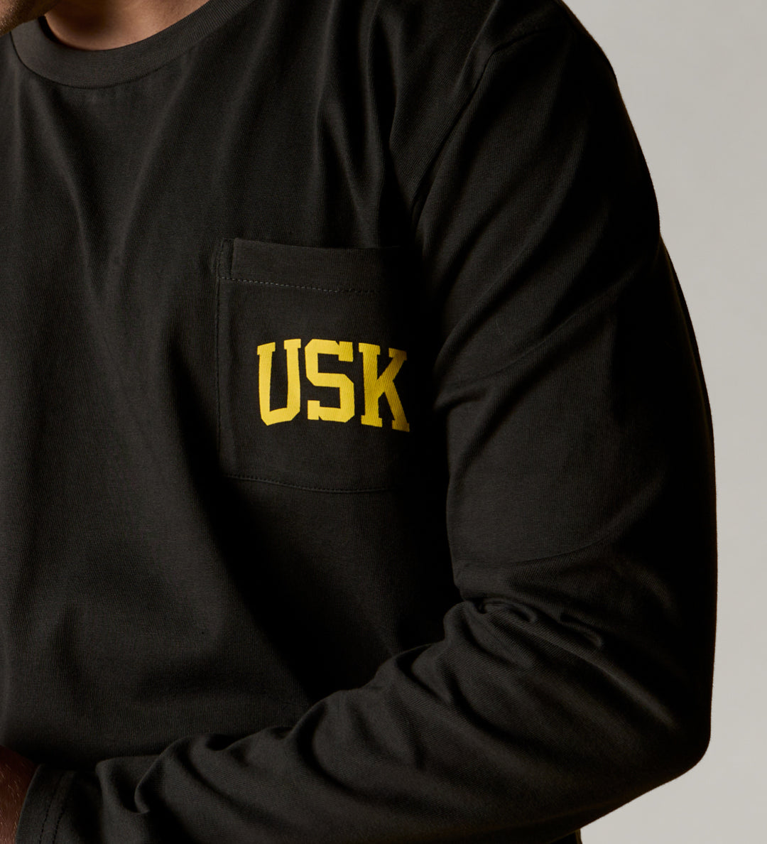 front model shot of the uskees faded black long sleeved Tee for men showing the bright yellow USK logo on the chest pocket