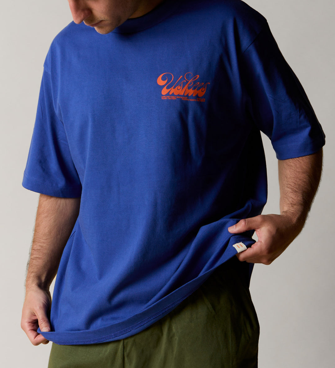 Front model shot of uskees ultra blue relaxed fit graphic Tee for men showing the 'Diner' design in orange