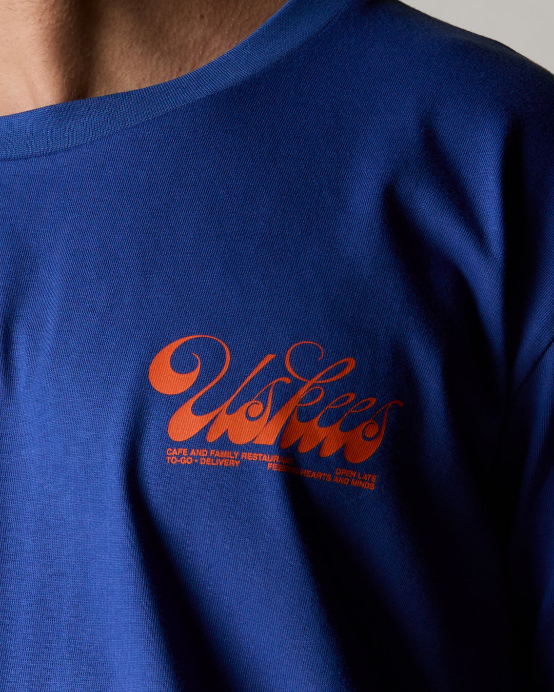  Close up shot of model wearing the uskees ultra blue baggy fit graphic Tee for men showing the 'Diner' design in orange