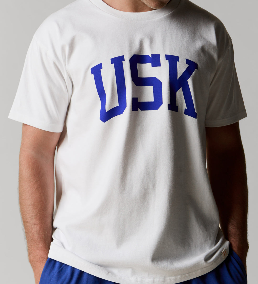 Model shot showing front of Uskees men's white short sleeve t-shirt with the signature USK logo on the front in blue.