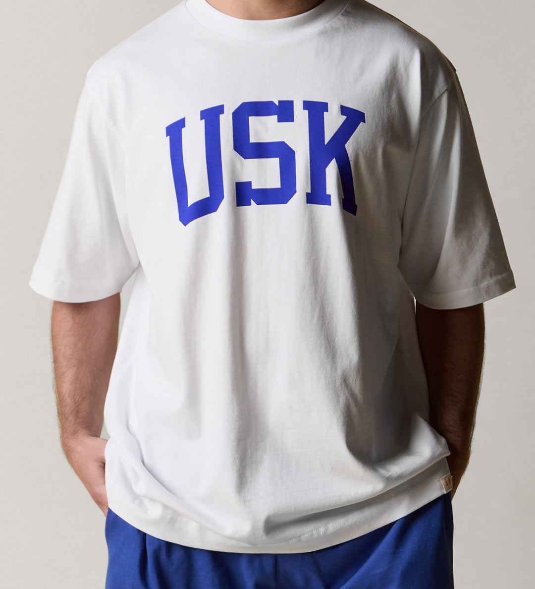 front  model shot of uskees signature relaxed fit T-shirt in white with an ultra blue USK logo 