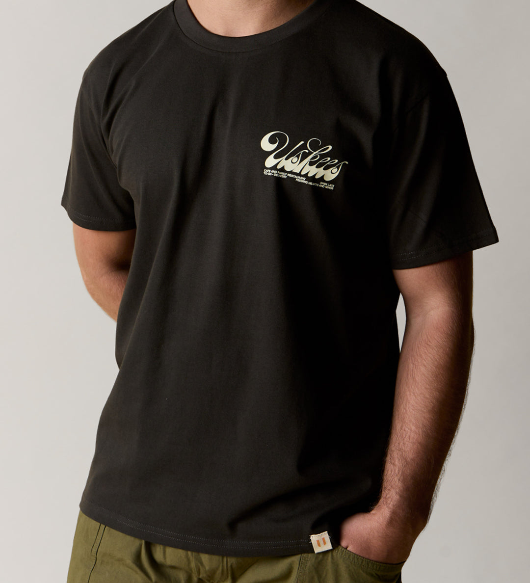 front model shot of uskees men's short sleeve graphic Tee in faded black showing the 'diner' logo in cream