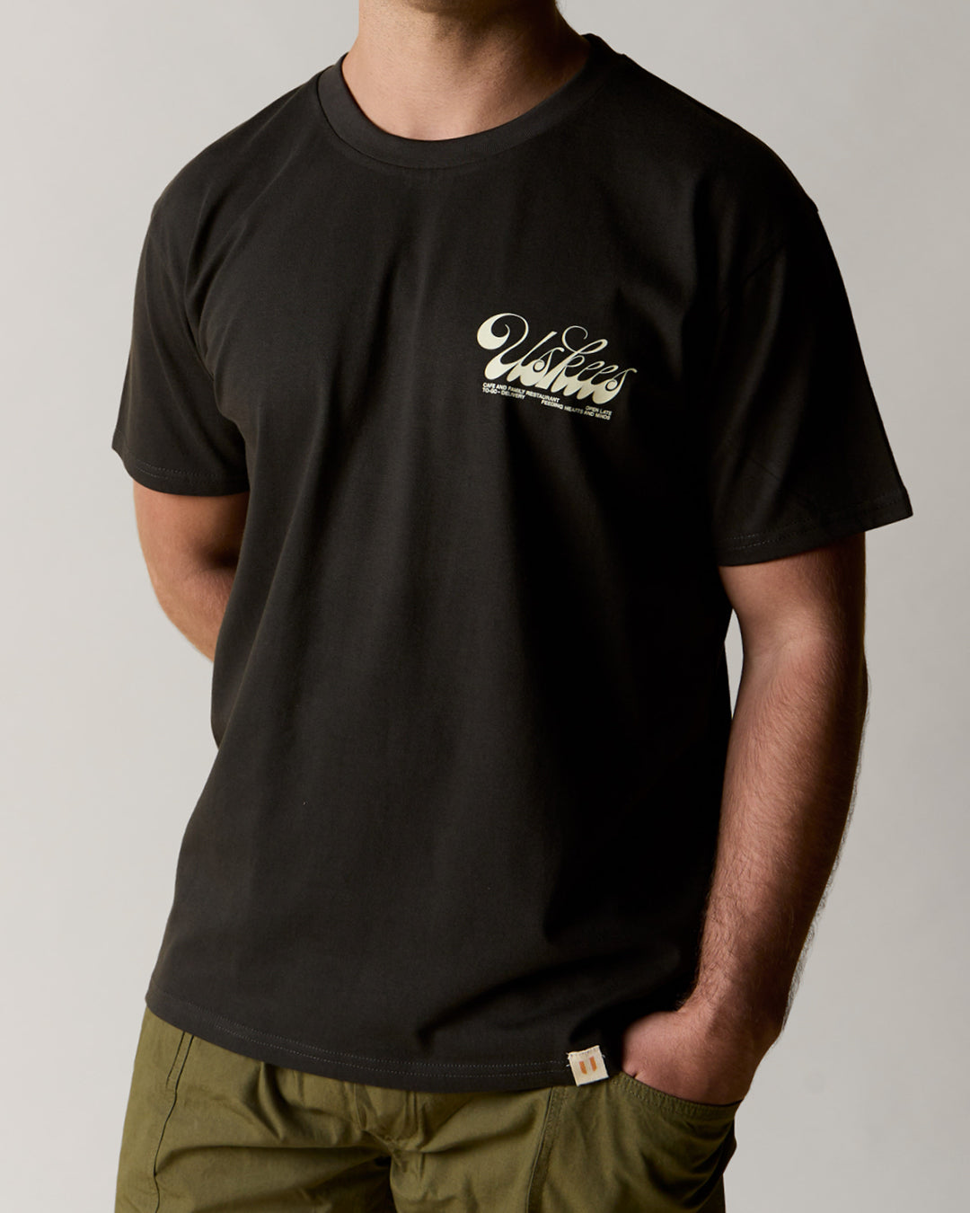 front model shot of uskees men's short sleeve graphic Tee in faded black showing the 'diner' logo in cream