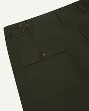 Back close view of #5014 Uskees men's organic cotton dark green cargo trousers showing belt loops, corozo buttons on pockets and adjuster buttons at waist.