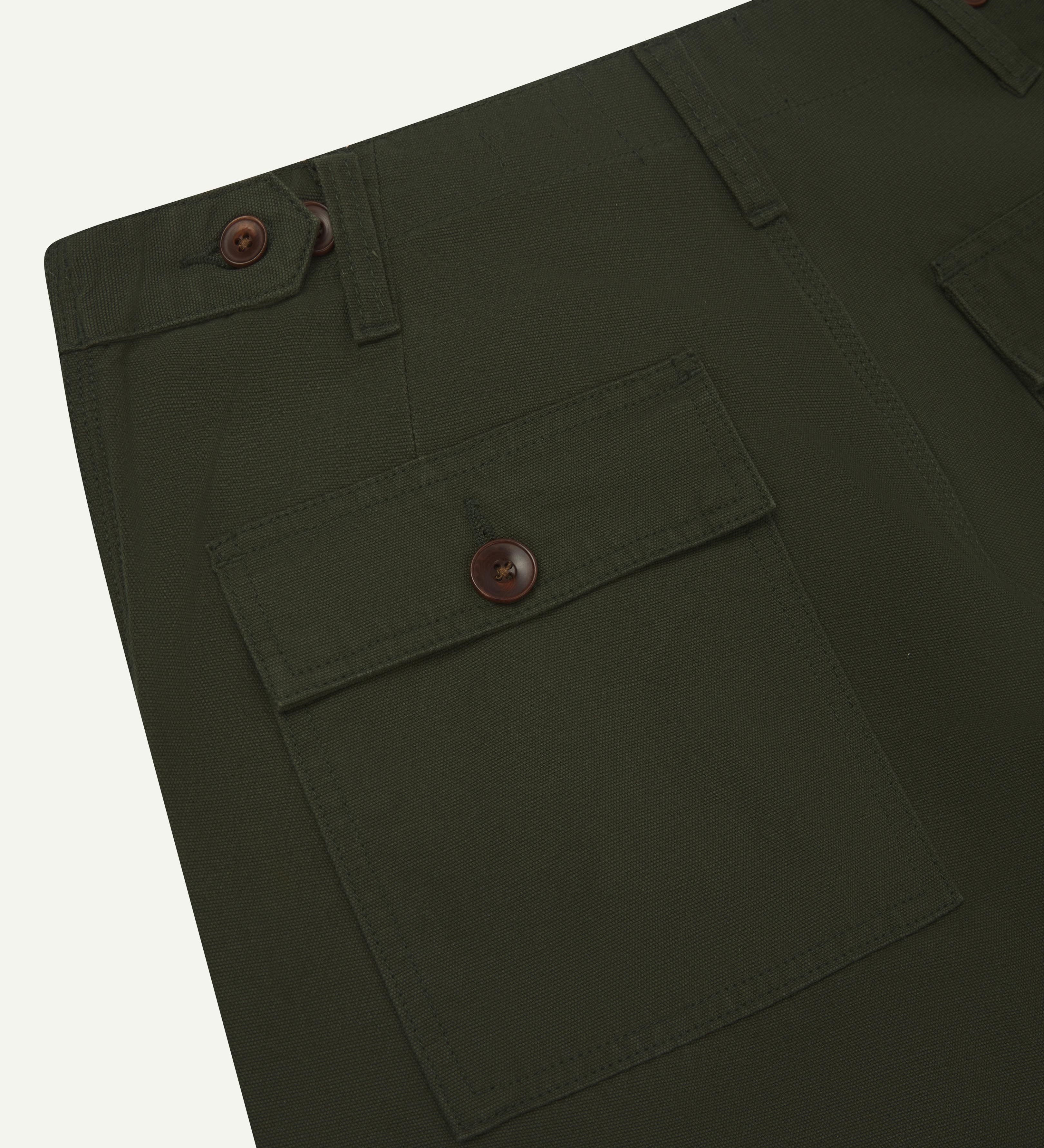Back close view of #5014 Uskees men's organic cotton dark green cargo trousers showing belt loops, corozo buttons on pockets and adjuster buttons at waist.