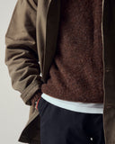 Close shot of a male model wearing an Uskees brown shacket, loam brown sweater, and dark blue trouserss on a plain background