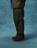 Man wearing Uskees ivy green ripstop utility pants and brown shoes on a textured blue background
