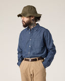 Model wearing Uskees blue chambray oxford shirt, khaki trousers and green hat.