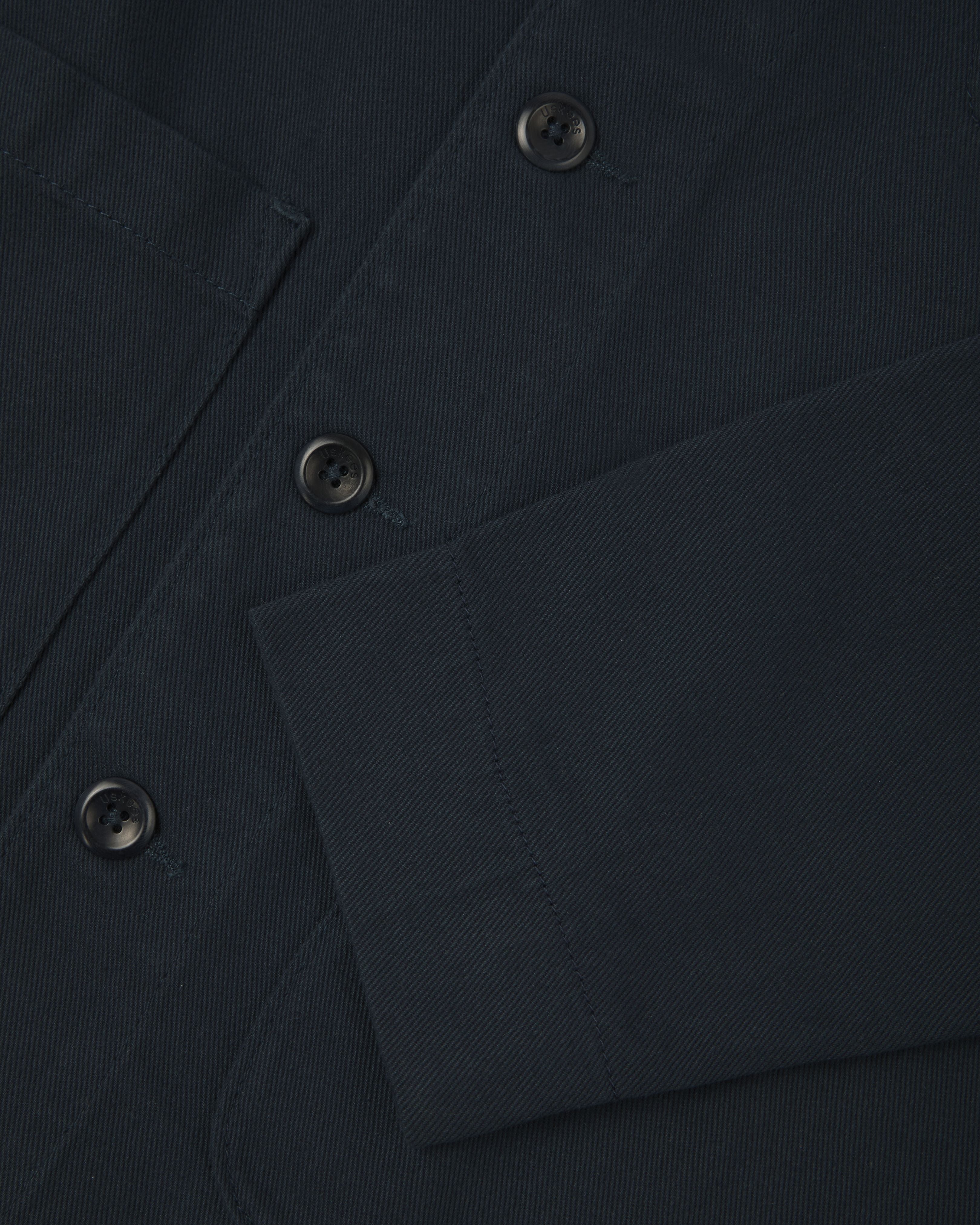 Close up view of dark blue organic cotton drill commuter blazer showing front buttons and cuff detail