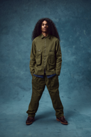 Male model wearing an Uskees green jacket and ivy green ripstop utility pants against a blue background