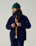 Male model wearing a deep indigo Uskees corduroy suit, green wool beanie, and glasses against a plain background