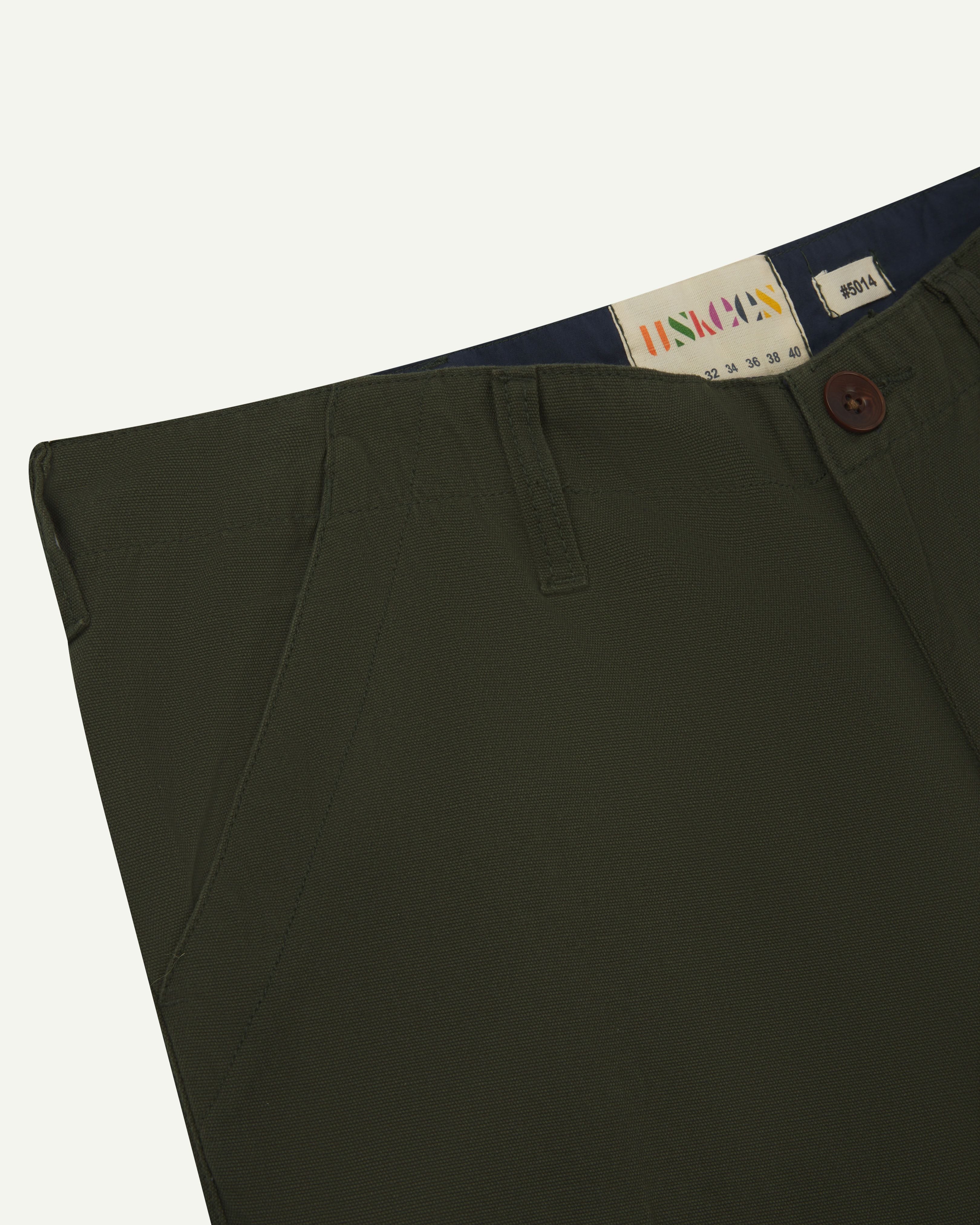 Close up view of #5014 Uskees men's organic cotton 'vine green' cargo trousers showing size label and front pocket