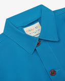 Close-up view of 3001 bright blue, buttoned organic cotton overshirt from Uskees showing corozo buttons, brand label, collar and hanging hoop.