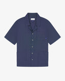Flat front view of mid blue organic chambray Cuban utility shirt from Uskees. Clearly showing 3 front pockets and corozo button front.
