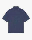 Flat back view of mid blue organic chambray Cuban utility shirt from Uskees with view of embroidered vents and loose, boxy shape.