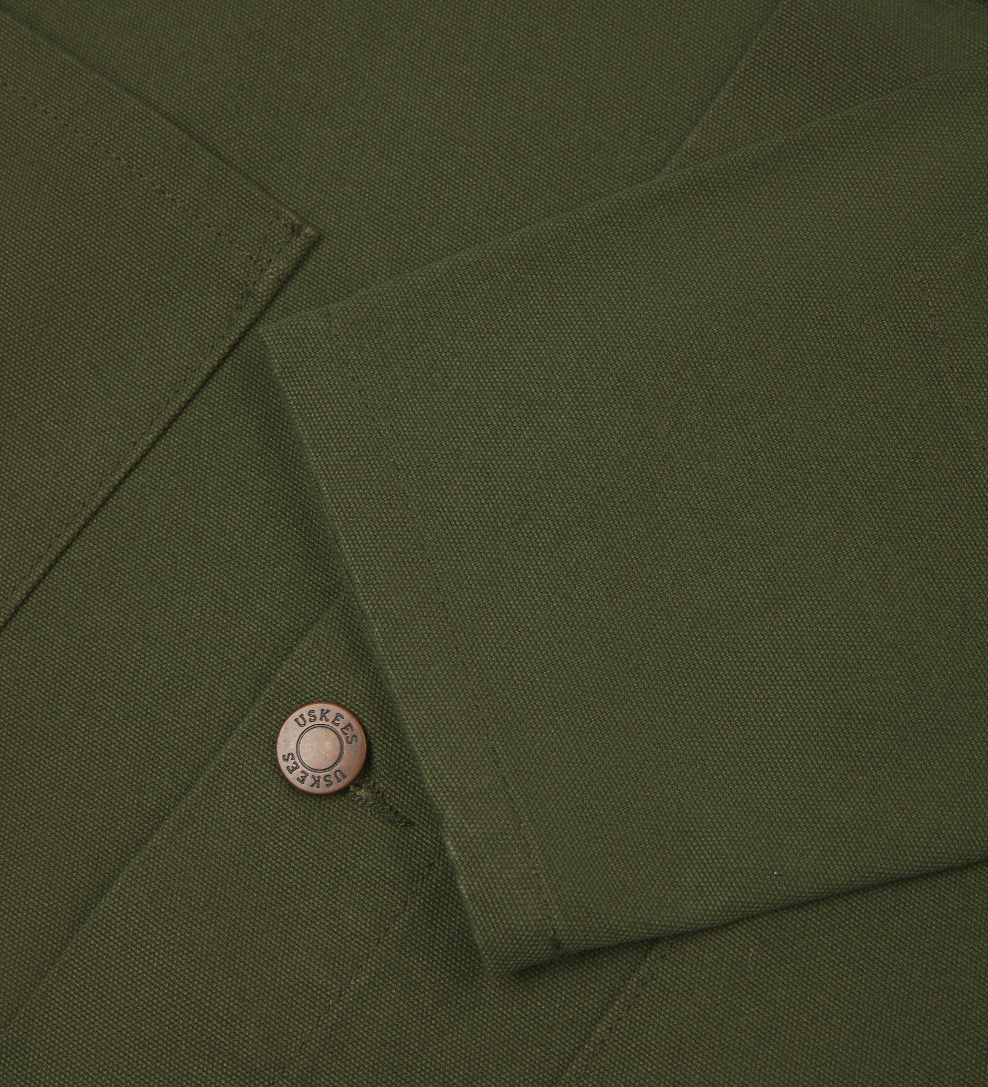Close-up view of uskees mid-green canvas men's overshirt presented buttoned up showing the sleeve cuff.