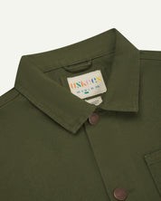 Close-up view of uskees mid-green canvas men's overshirt presented buttoned up showing the collar and brand/size label.