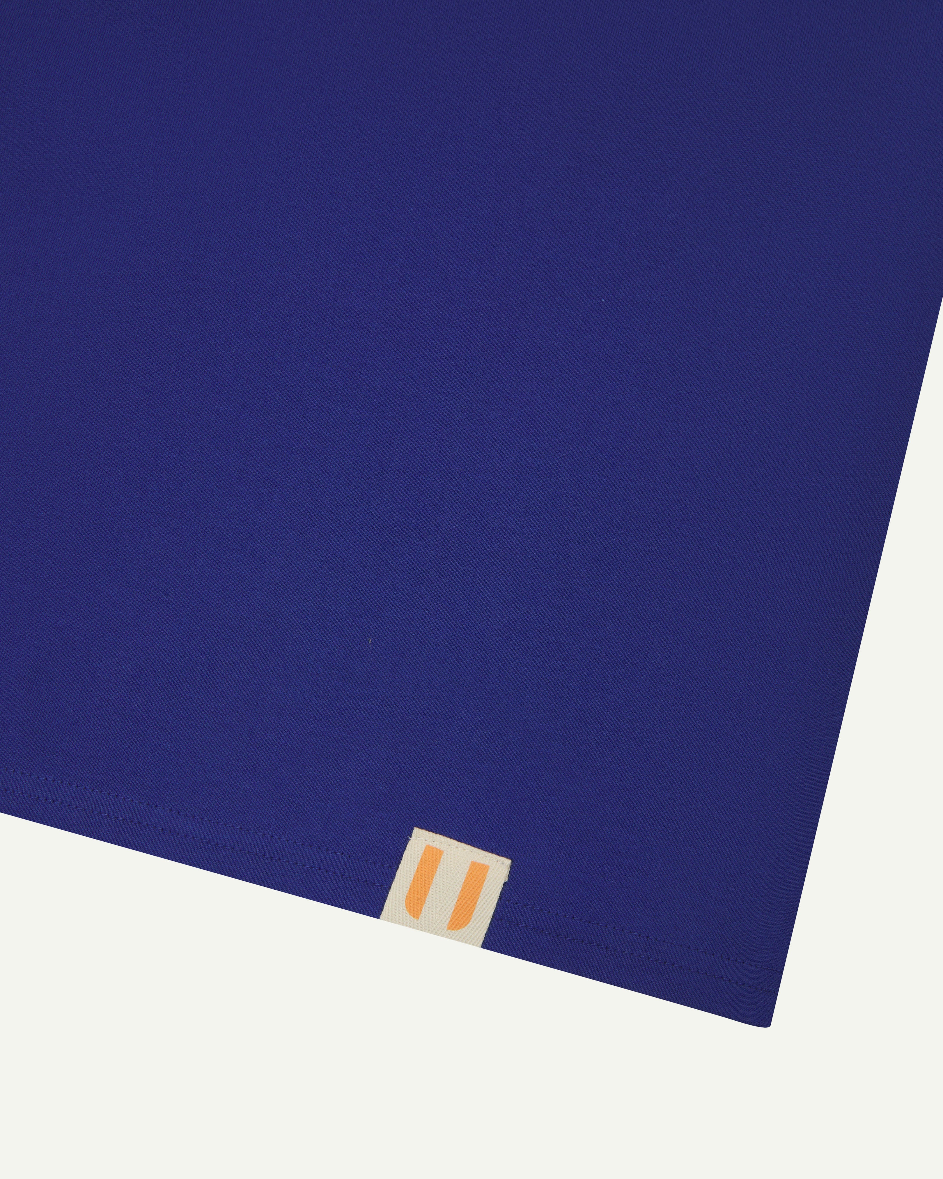 Close view of uskees #7006 men's short sleeve Tee in bright blue showing logo label at hem.
