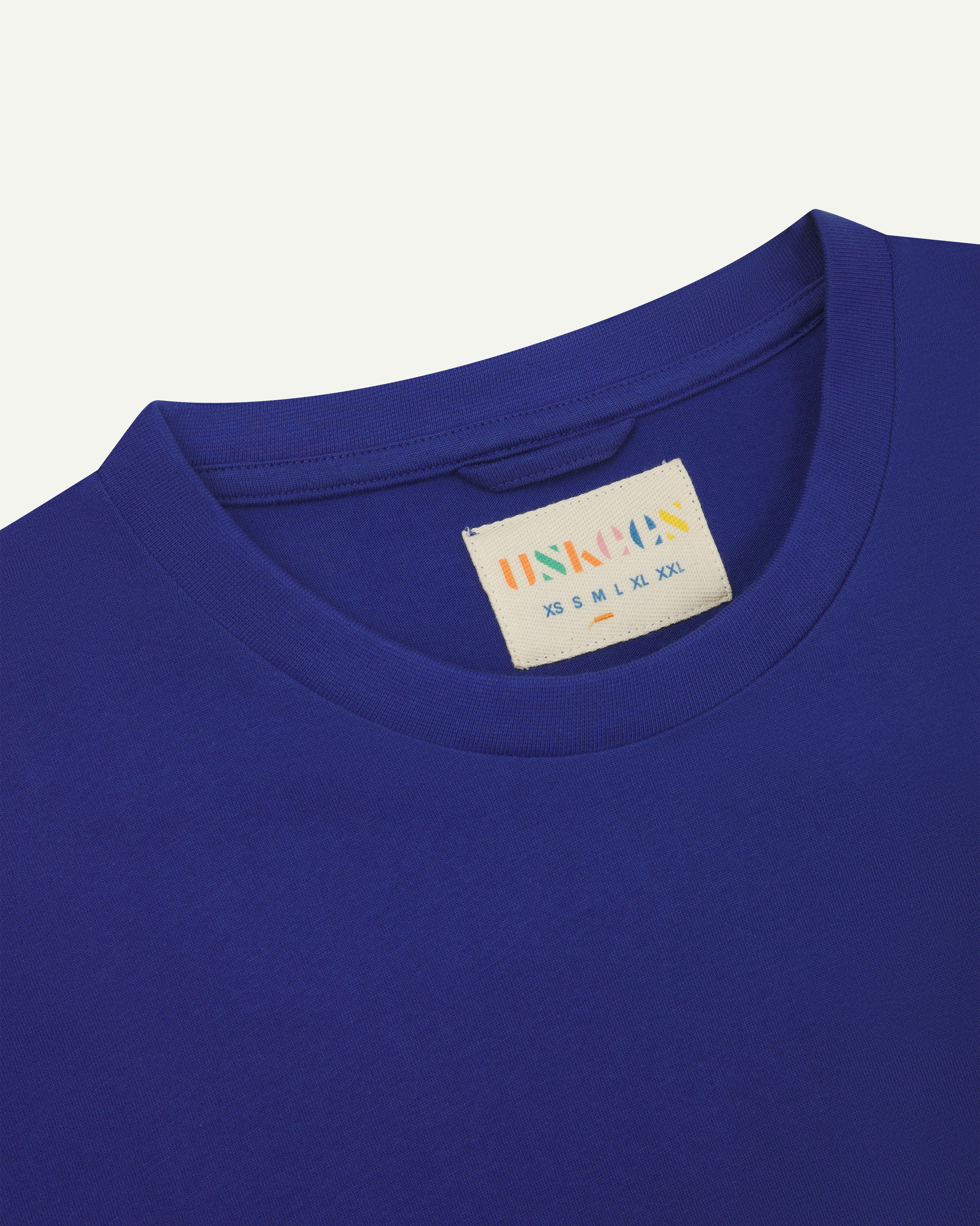 Front close-up view of uskees #7006 men's short sleeve T-shirt in bright blue showing the brand/size label at neck.