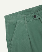 Front close-up view of #5018 Uskees men's organic corduroy boat trousers in light green showing belt loop, waist button fastening and slanted front pocket.