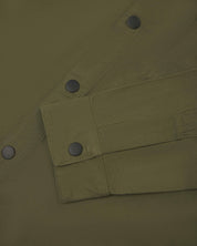 Close-up view of  men's olive green uskees lightweight shirt. Clear view of black popper fastening  on cuff and front of shirt.