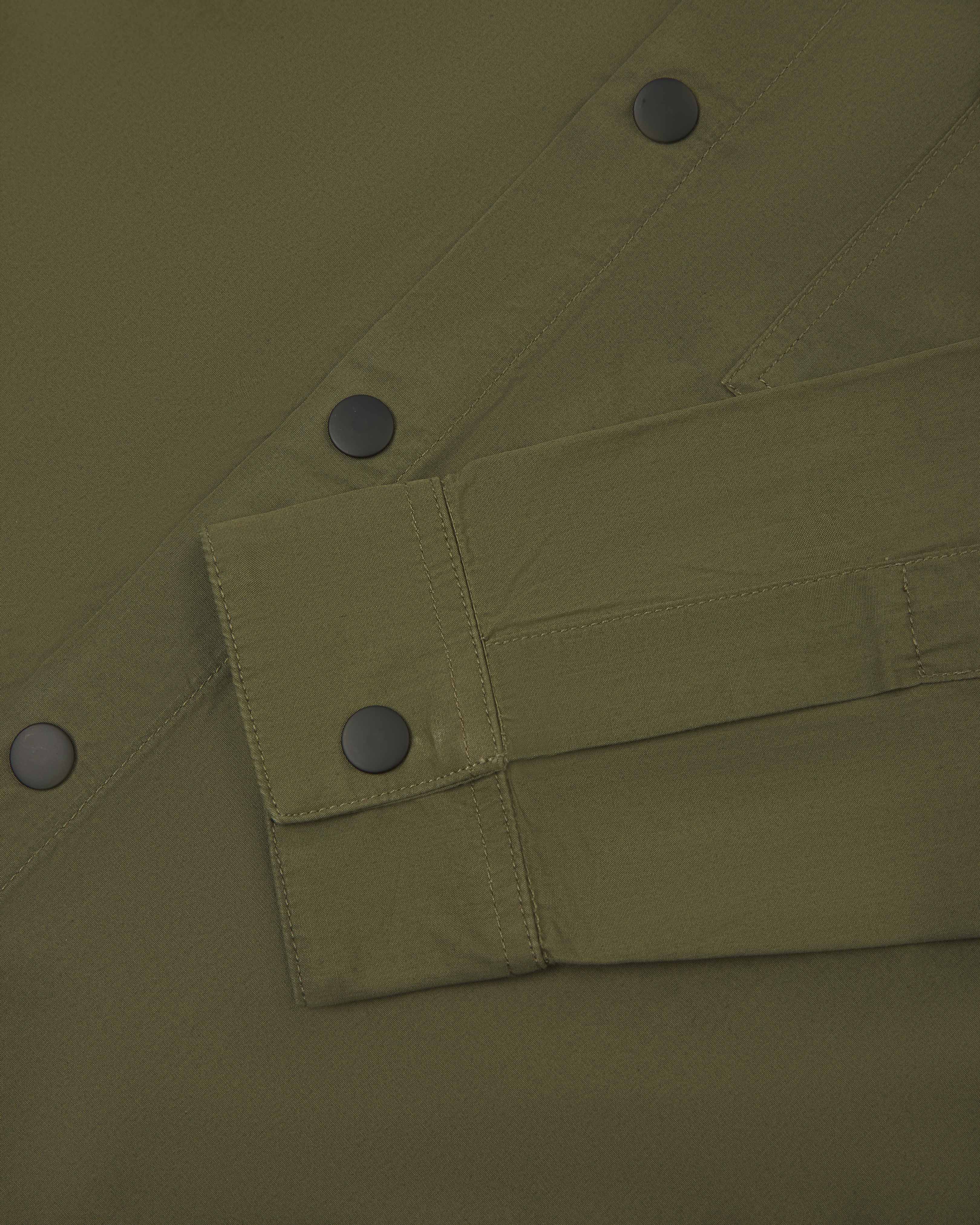 Close-up view of  men's olive green uskees lightweight shirt. Clear view of black popper fastening  on cuff and front of shirt.
