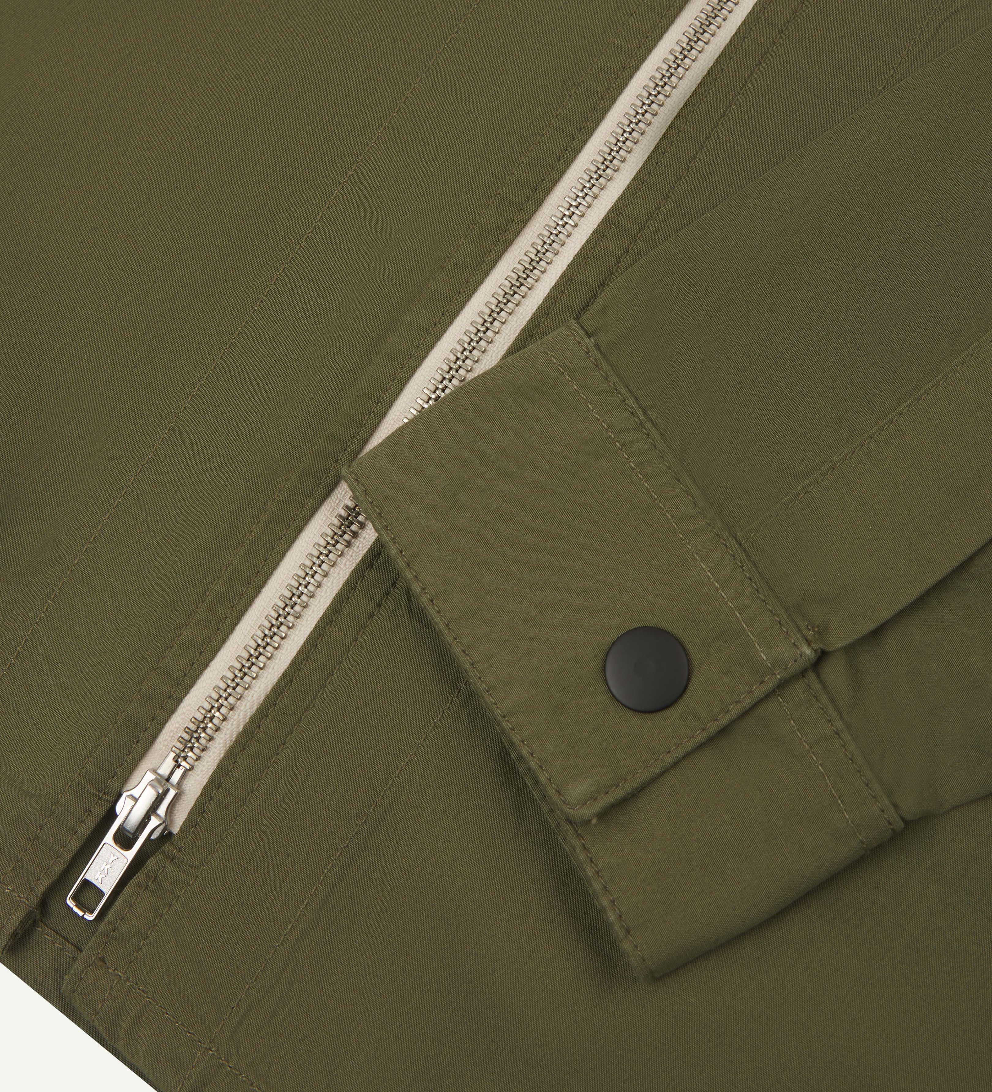 Close-up view of uskees zip front lightweight men's jacket in olive green showing the contrast zip and black popper fastening on cuff.