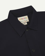 front close shot of uskees dark blue men's shirt with short sleeves showing black popper fastenings and colourful brand/size label