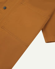 Close-up shot of uskees lightweight tan men's shirt with short sleeves showing black popper fastening and chest pocket.