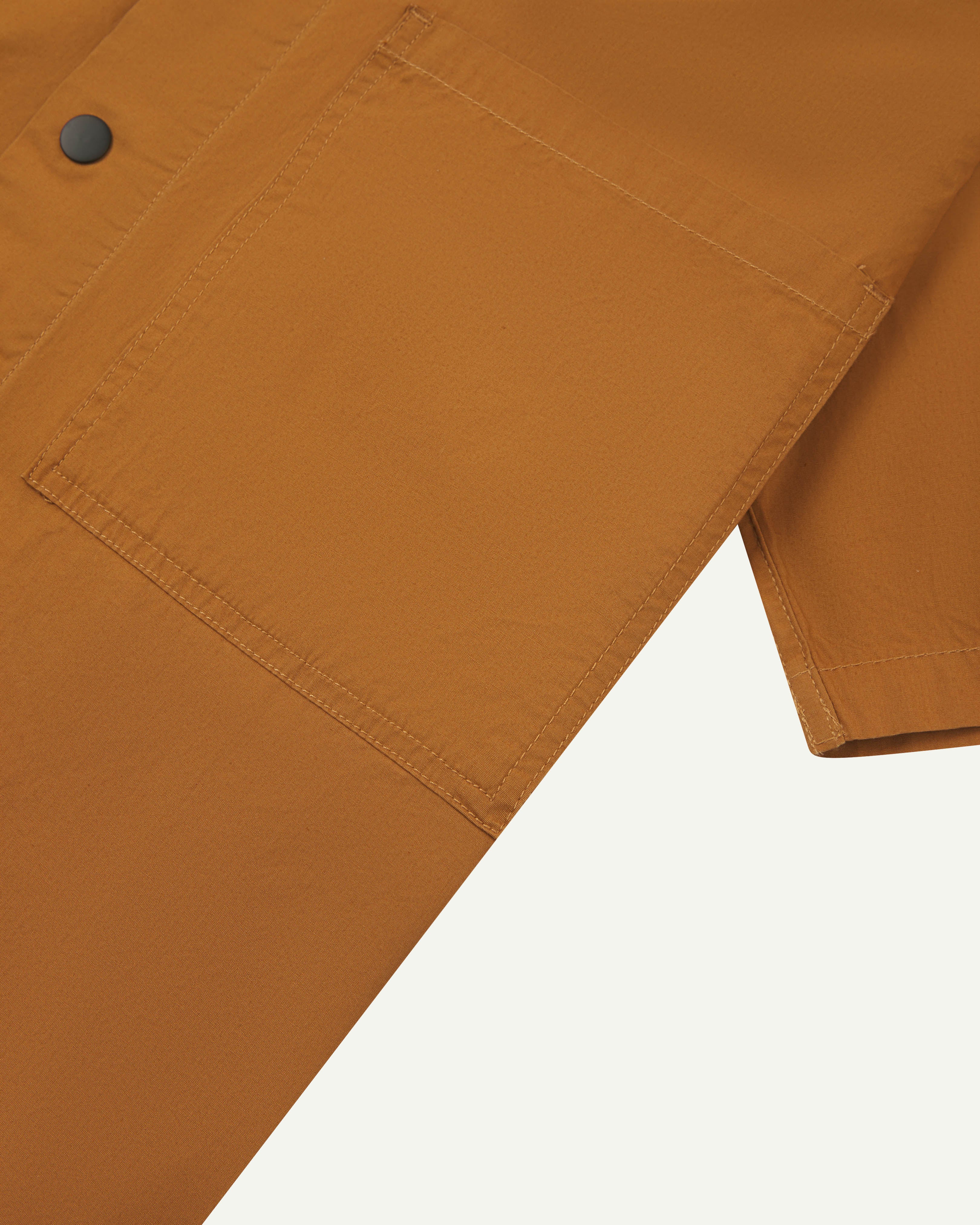 Close-up shot of uskees lightweight tan men's shirt with short sleeves showing black popper fastening and chest pocket.