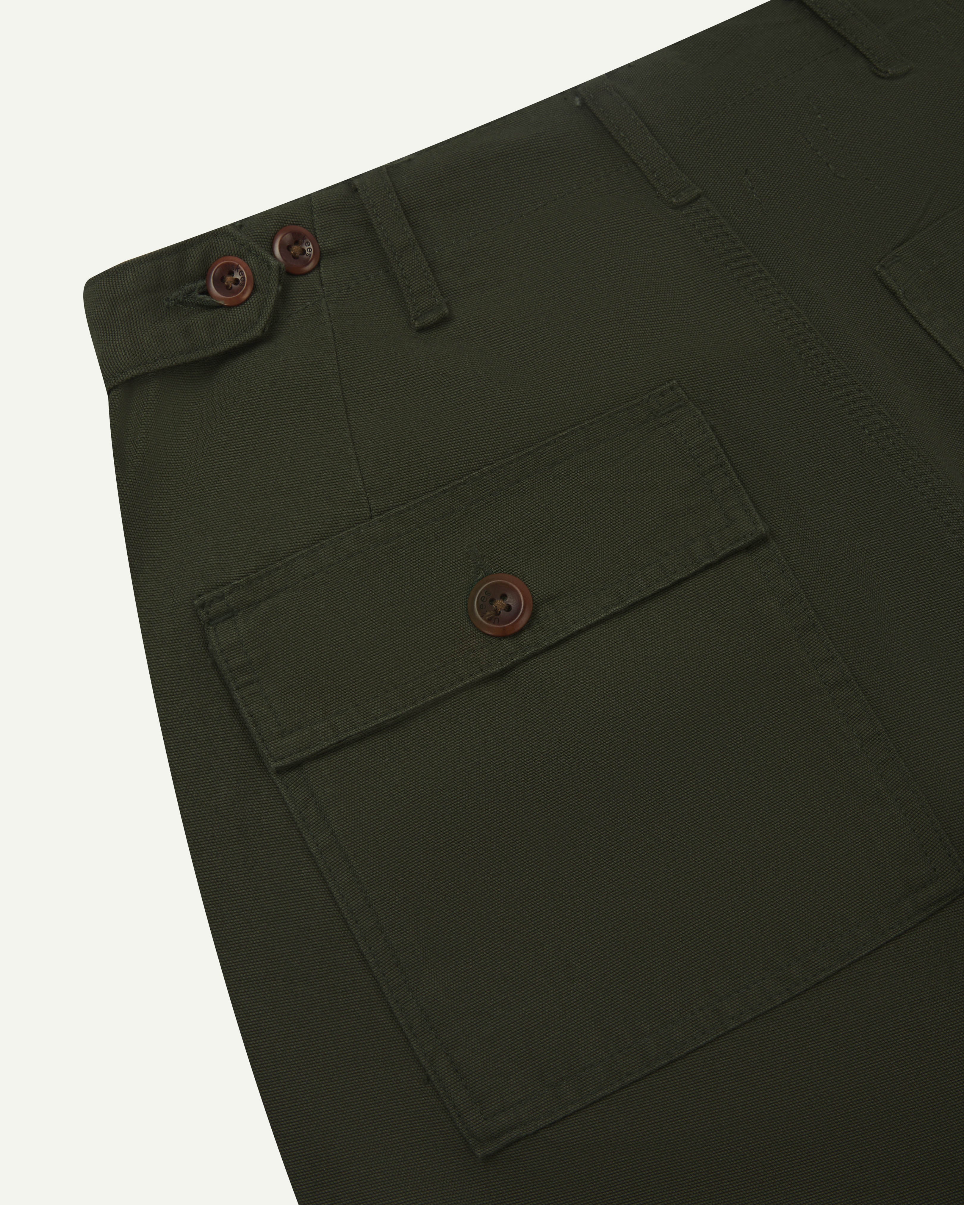 Close-up view of Uskees vine green work pants with focus on natural corozo buttons, left rear pocket, belt loops, triple stitching and adjustable button waist.