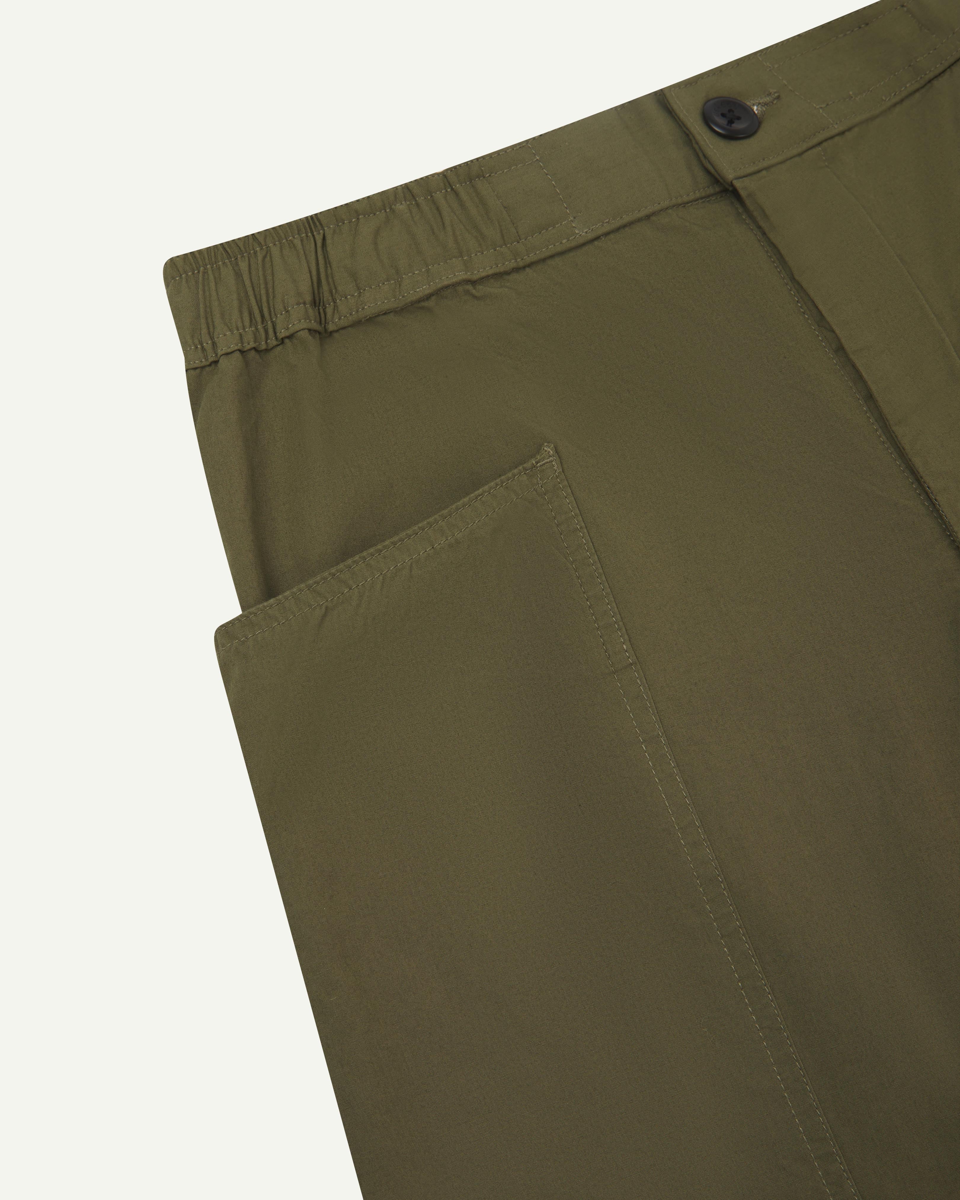 Close angled view of the elasticated waist and corozo button fastening of the olive green #5011 Uskees pants.