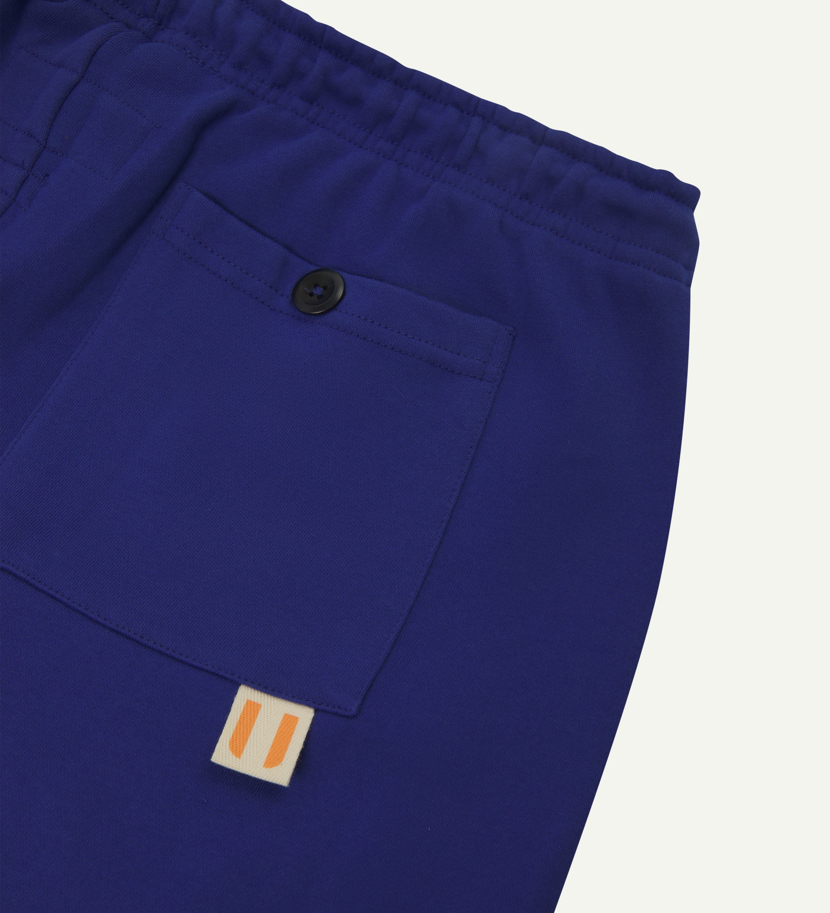 Back close view of bright blue organic cotton Jogging Pants for men by Uskees showing buttoned back pocket and logo label.