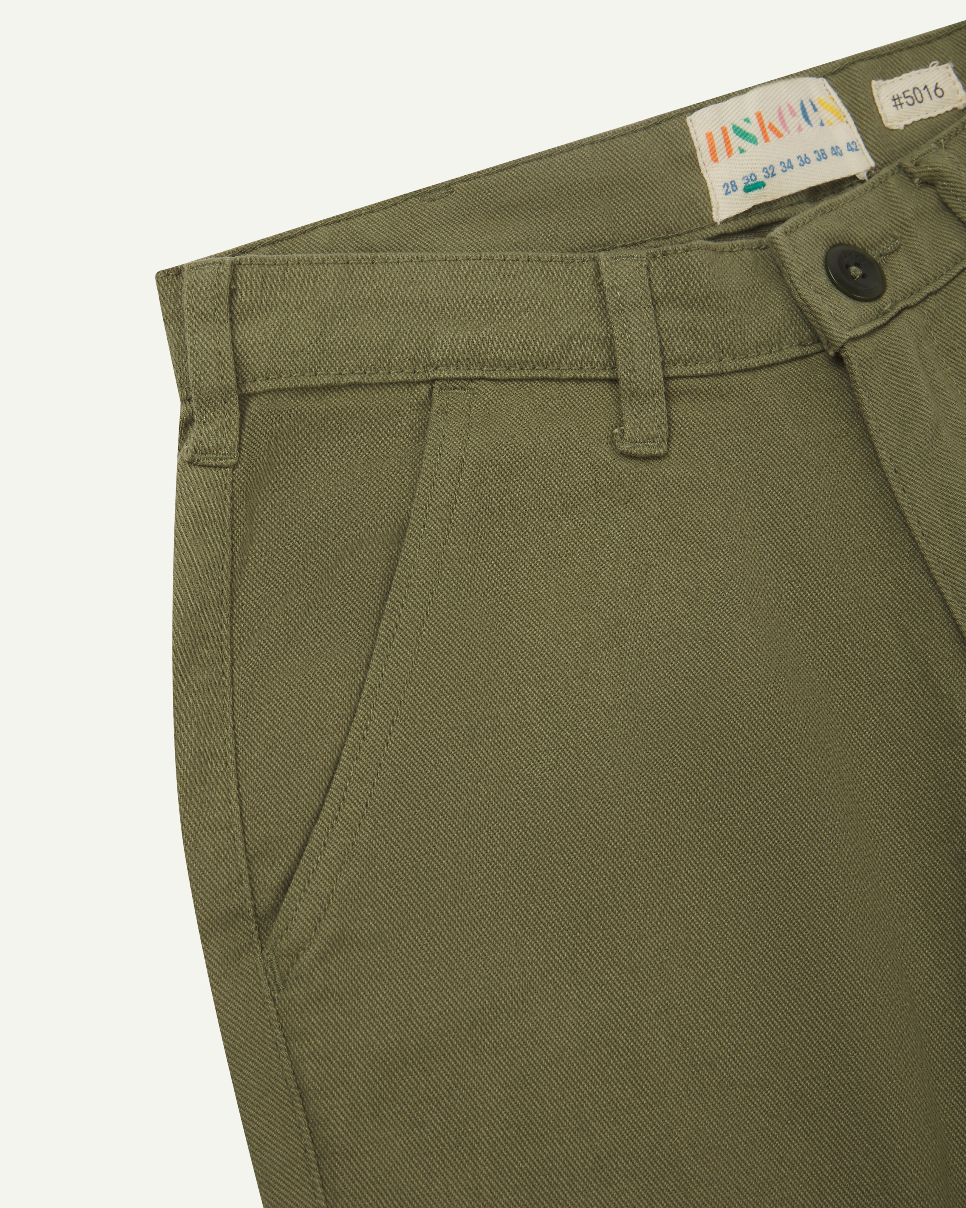 Front close view of uskees cotton drill 'commuter' trousers for men in moss green showing belt loops, front pocket and brand label at waist