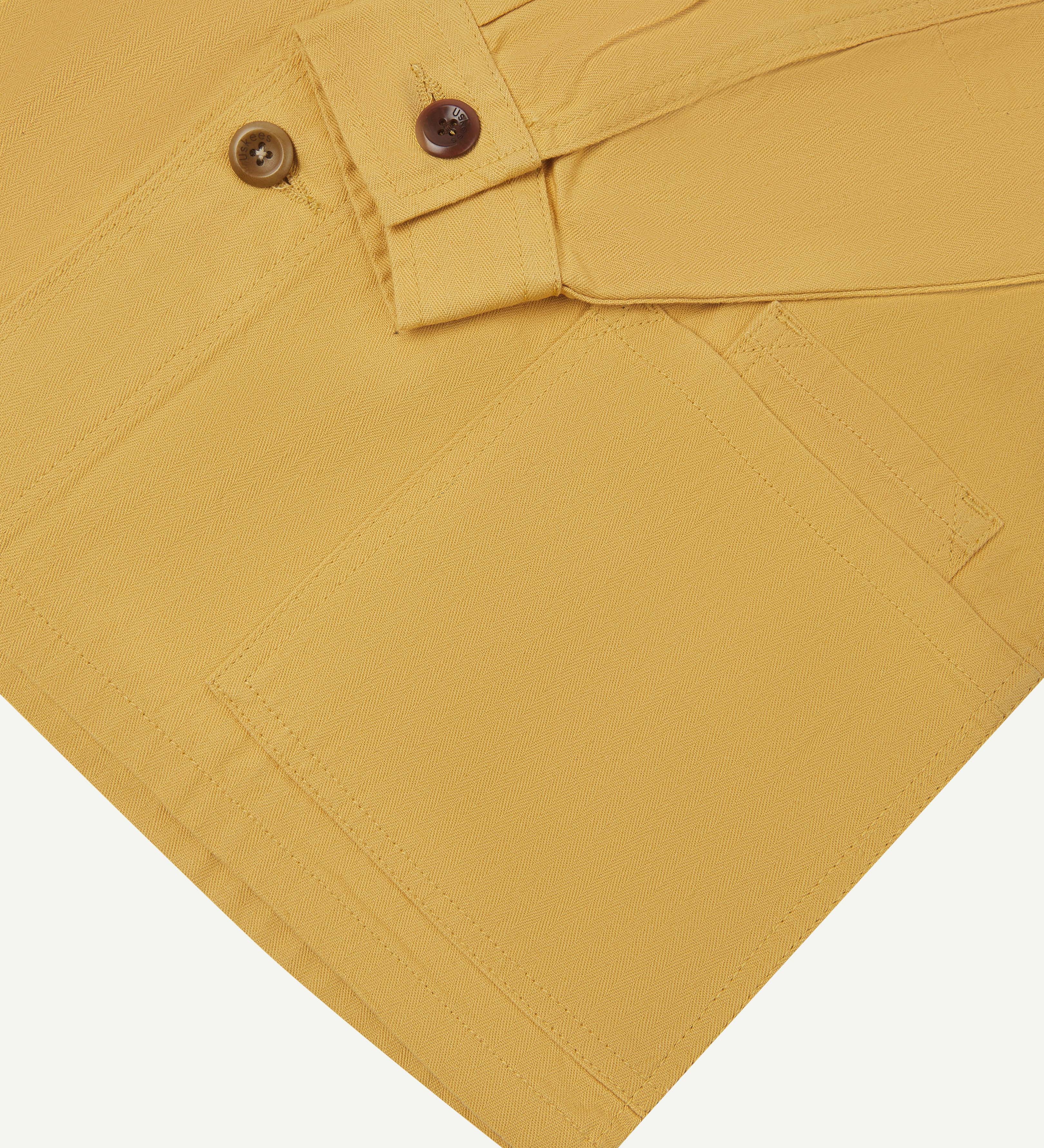 Close up shot of Uskees sandstone organic herringbone cotton engineer jacket showing cuff detail and corozo buttons.