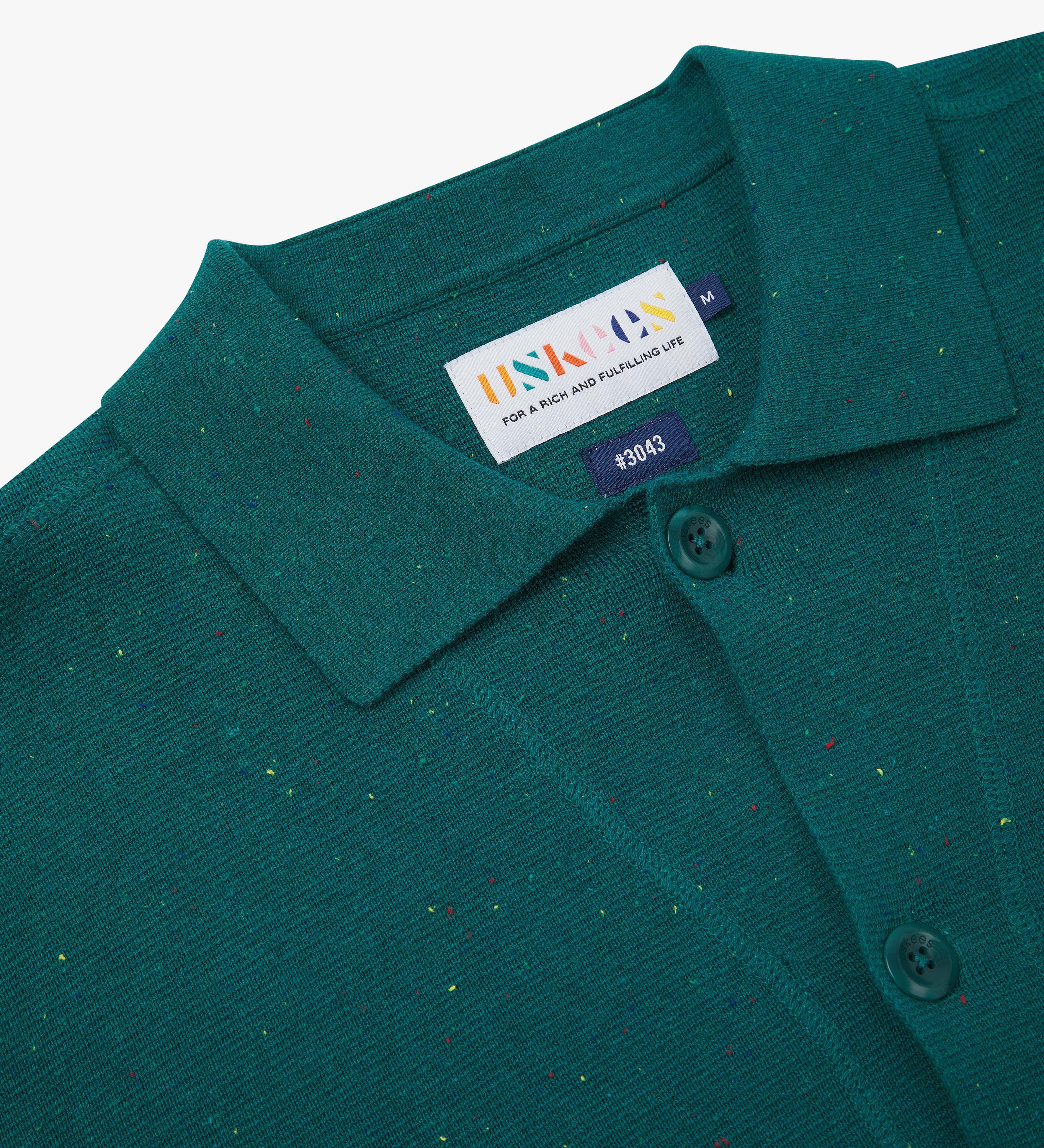 Close-up front view of knitted organic cotton foam green cardigan showing the collar, corozo buttons and Uskees brand label.