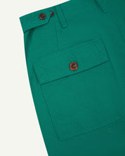 Close-up angled view of Uskees foam green coloured cotton work pants with focus on natural corozo buttons, left rear pocket, belt loops, triple stitching and adjustable button waist.