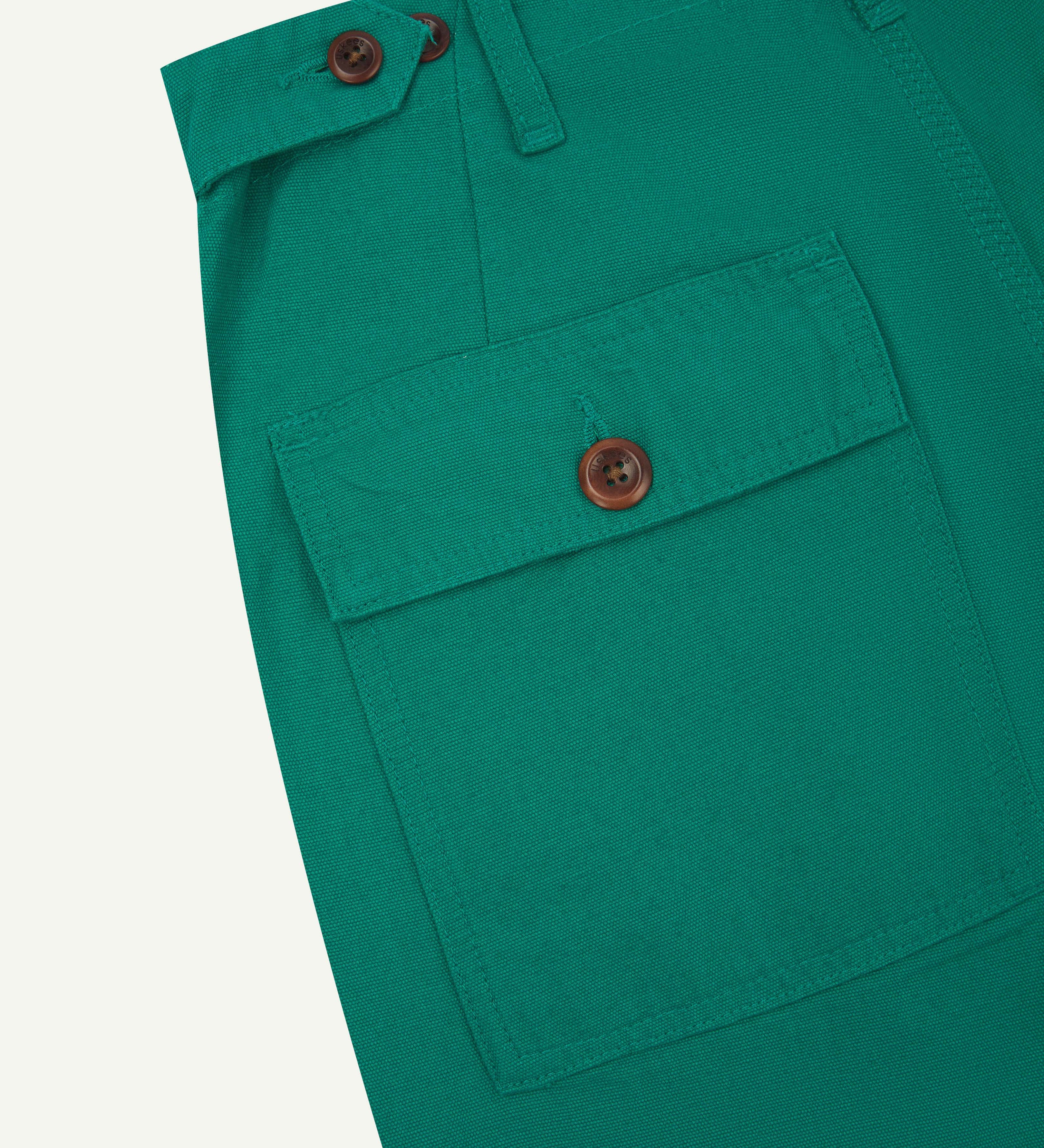 Close-up angled view of Uskees foam green coloured cotton work pants with focus on natural corozo buttons, left rear pocket, belt loops, triple stitching and adjustable button waist.