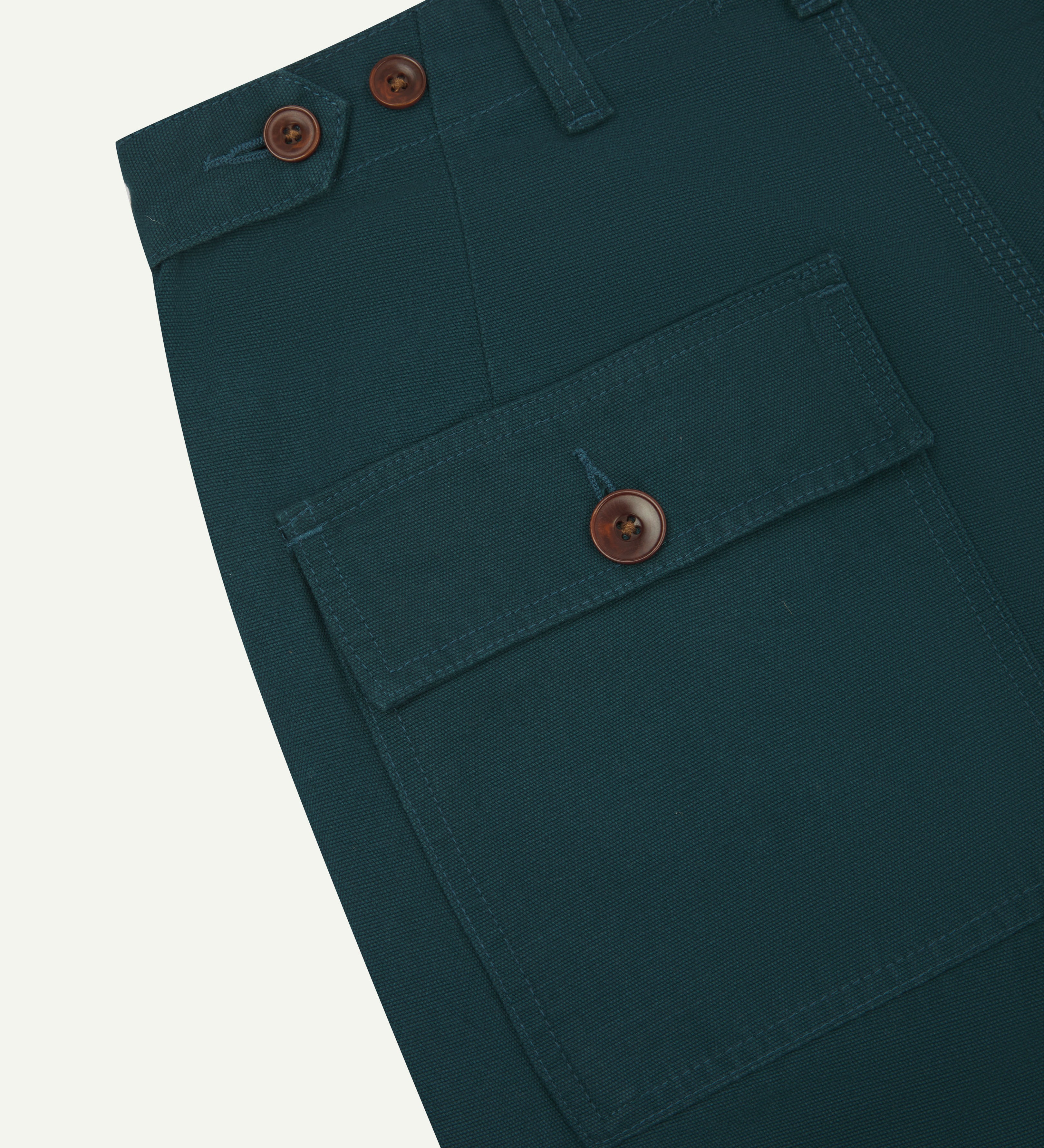 Close-up angled view of Uskees peacock coloured cotton work pants with focus on natural corozo buttons, left rear pocket, belt loops, triple stitching and adjustable button waist.