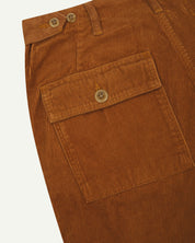 Angled, close-up view of Uskees tan corduroy work pants with focus on natural corozo buttons, left rear pocket, belt loops, triple stitching and adjustable button waist.